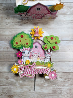 Decorative cake topper with farm-themed design, barn, trees, and animals on a wooden surface.
